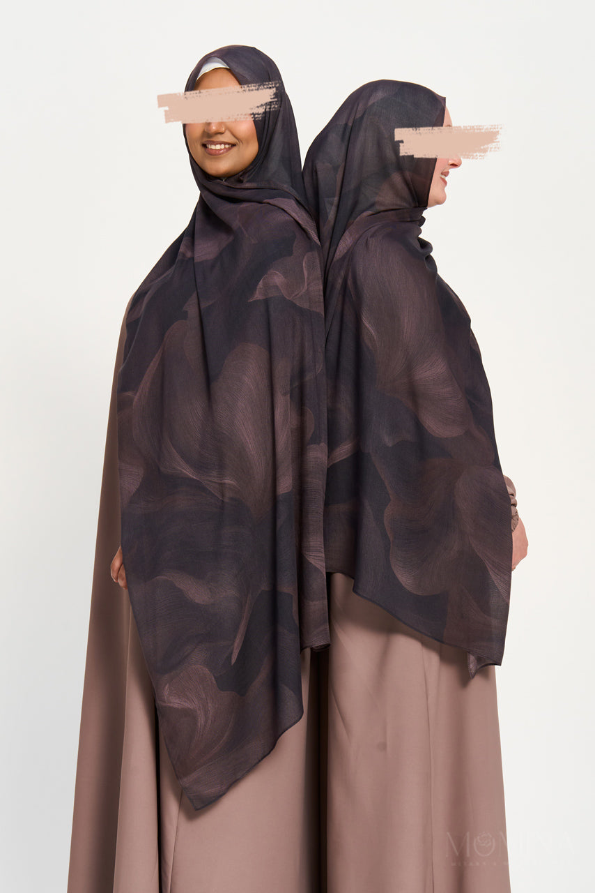 Woman wearing a dark patterned hijab and beige dress on a white background