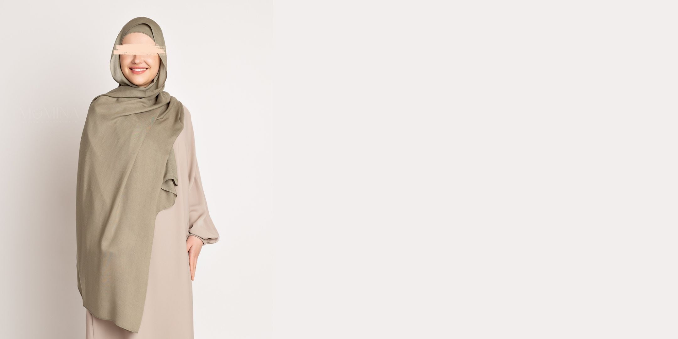 A muslim woman wearing a muted green colored modal hijab with a beige abaya from momina hijabs - Front pose photograph with a solid off-white background. 