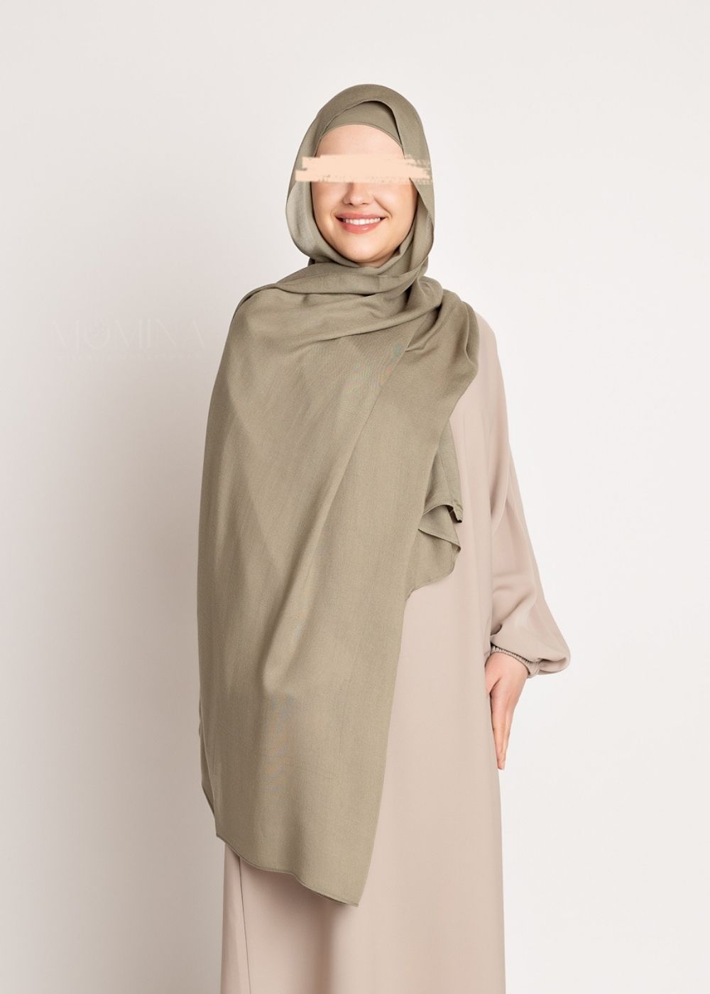 A muslim woman wearing a muted green colored Modal hijab with a matching undercap from momina hijabs. Full body shot front pose with a solid soft white background